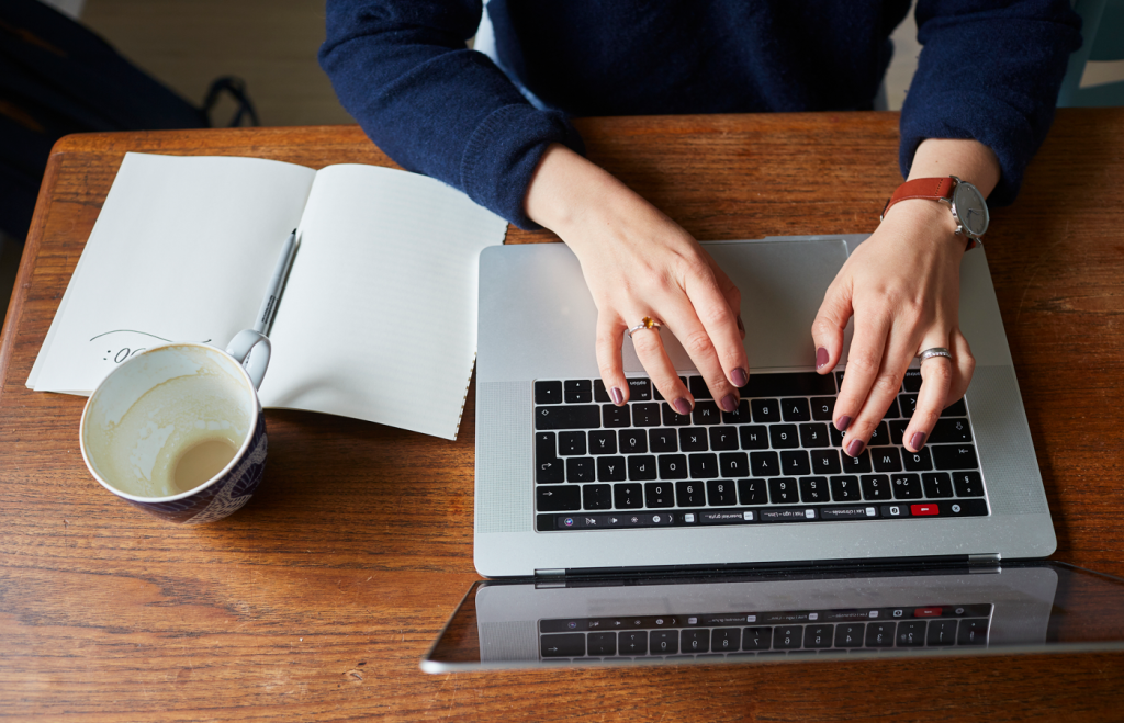 Kvinnas händer som skriver på datorn, kaffekopp, anteckingsblock.